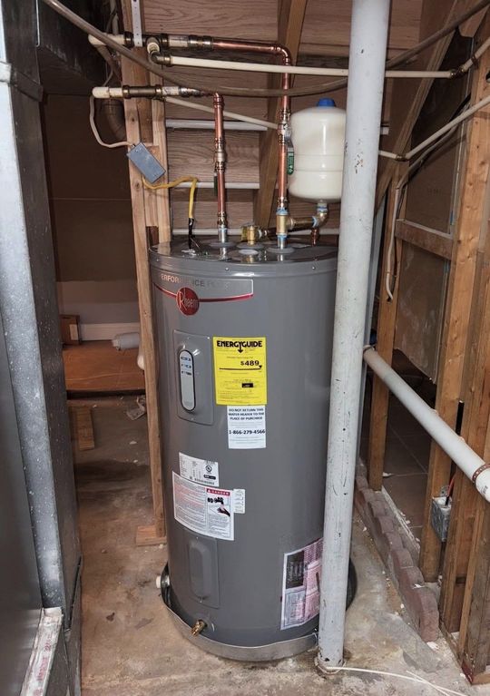 Gray water heater in a narrow utility closet with exposed pipes and wood framing.