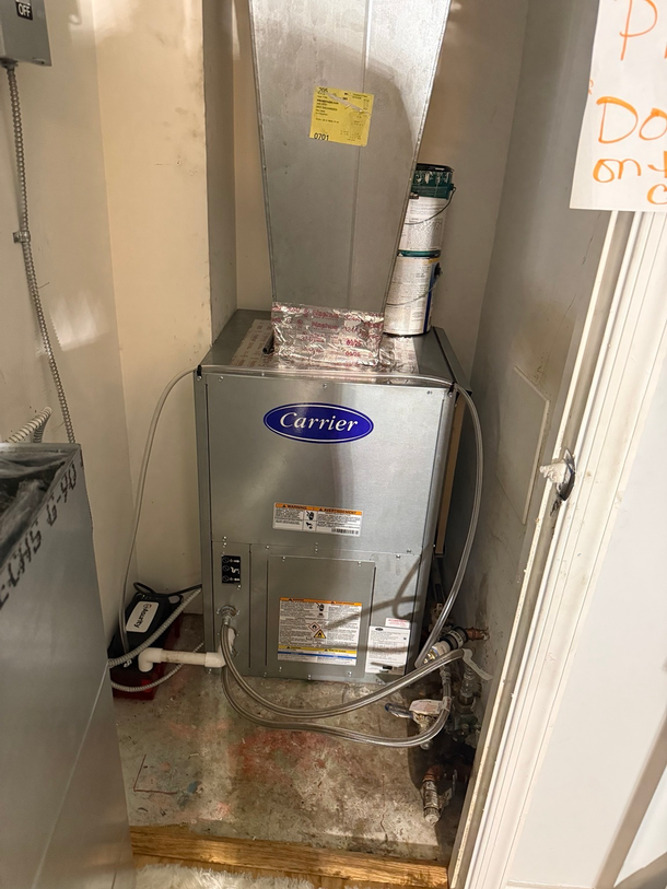 Gas furnace in a narrow utility closet with exposed ducting and pipes.