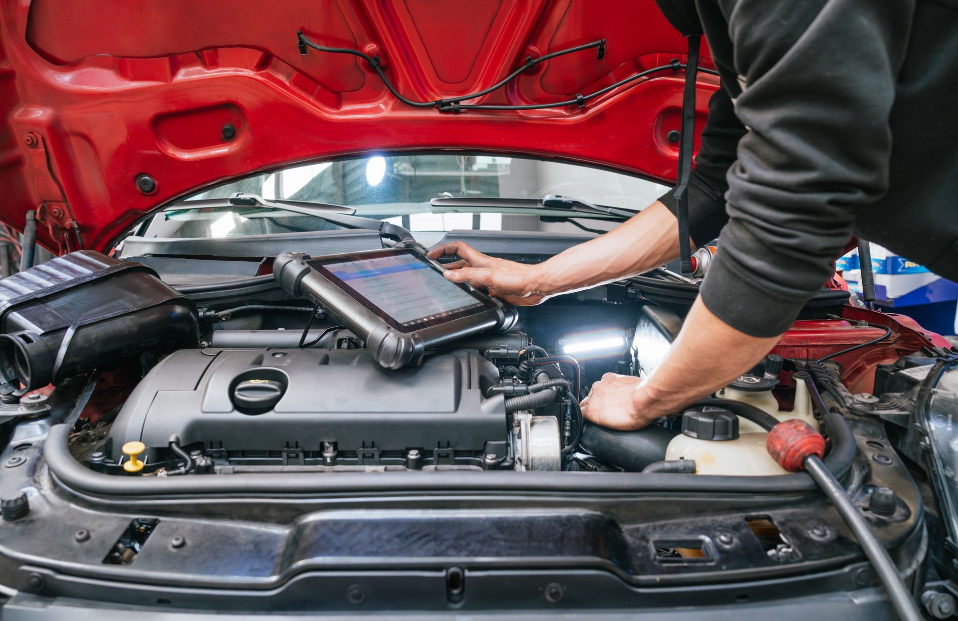 Mechanic using a diagnostic tablet to inspect a car engine under a red hood | Apex Auto Care