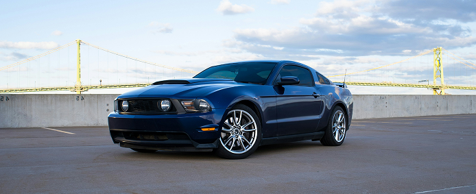 Dark blue sports car parked on a bridge with yellow suspension cables in the background