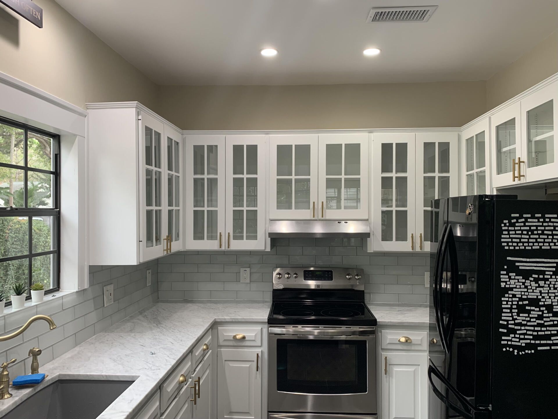 A modern kitchen featuring white glass-front cabinets, a marble countertop, light gray subway tile backsplash, and a stove.