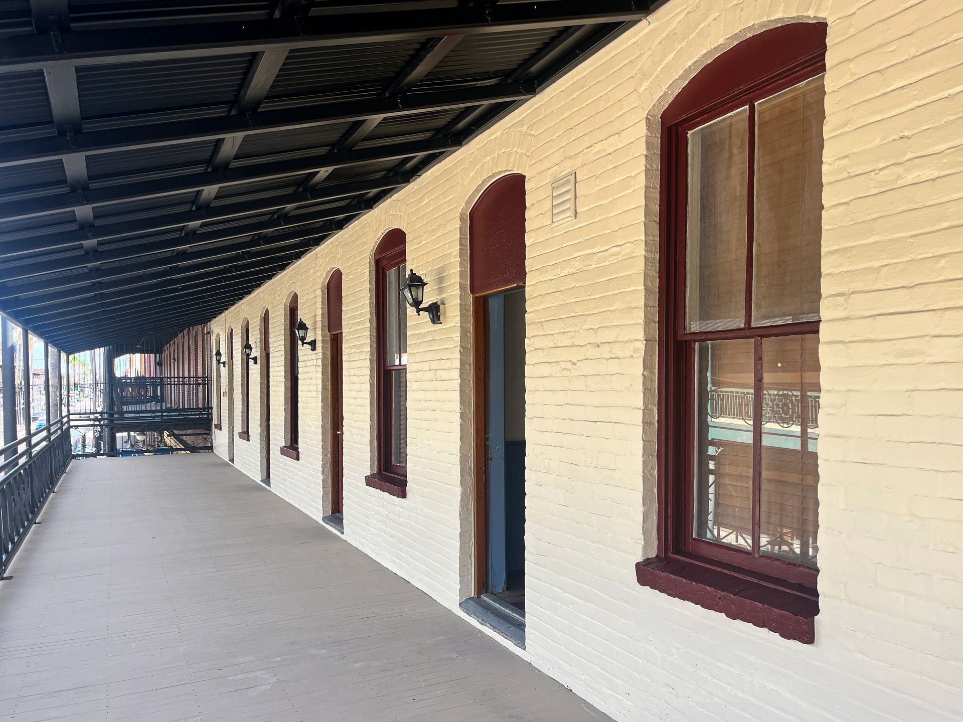 A long covered porch with cream brick walls, arched dark red window frames, and doors stretching down a hallway.