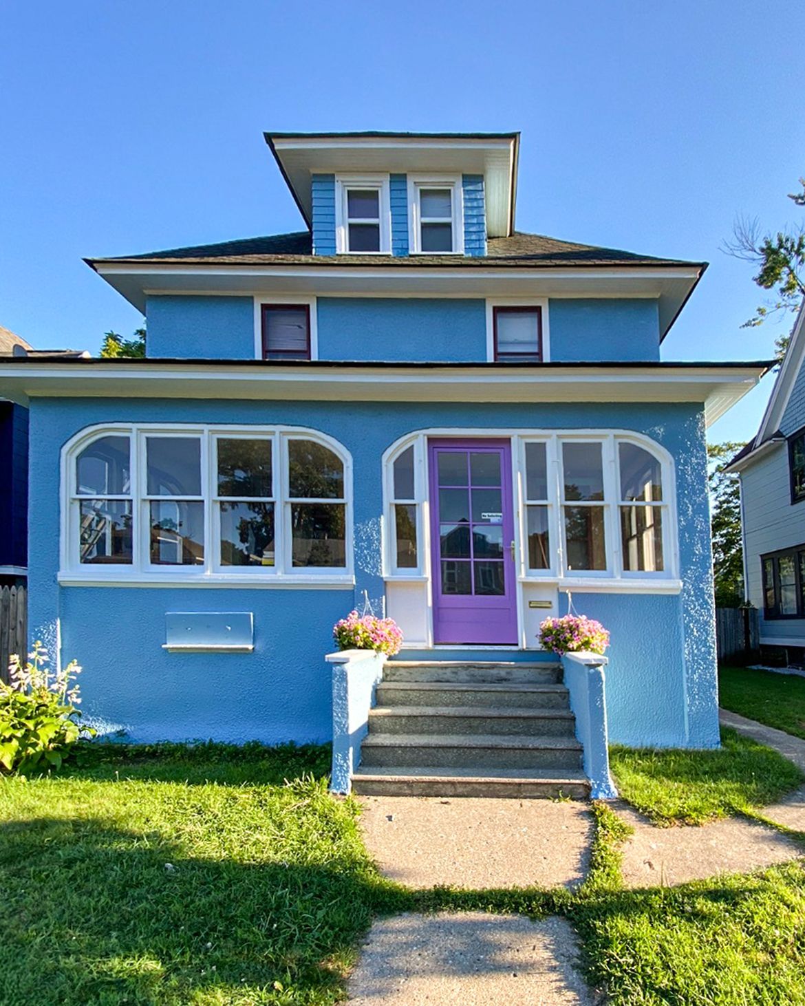 A bright blue two-story house with a purple front door, white-trimmed windows, a small front porch, and a yard.