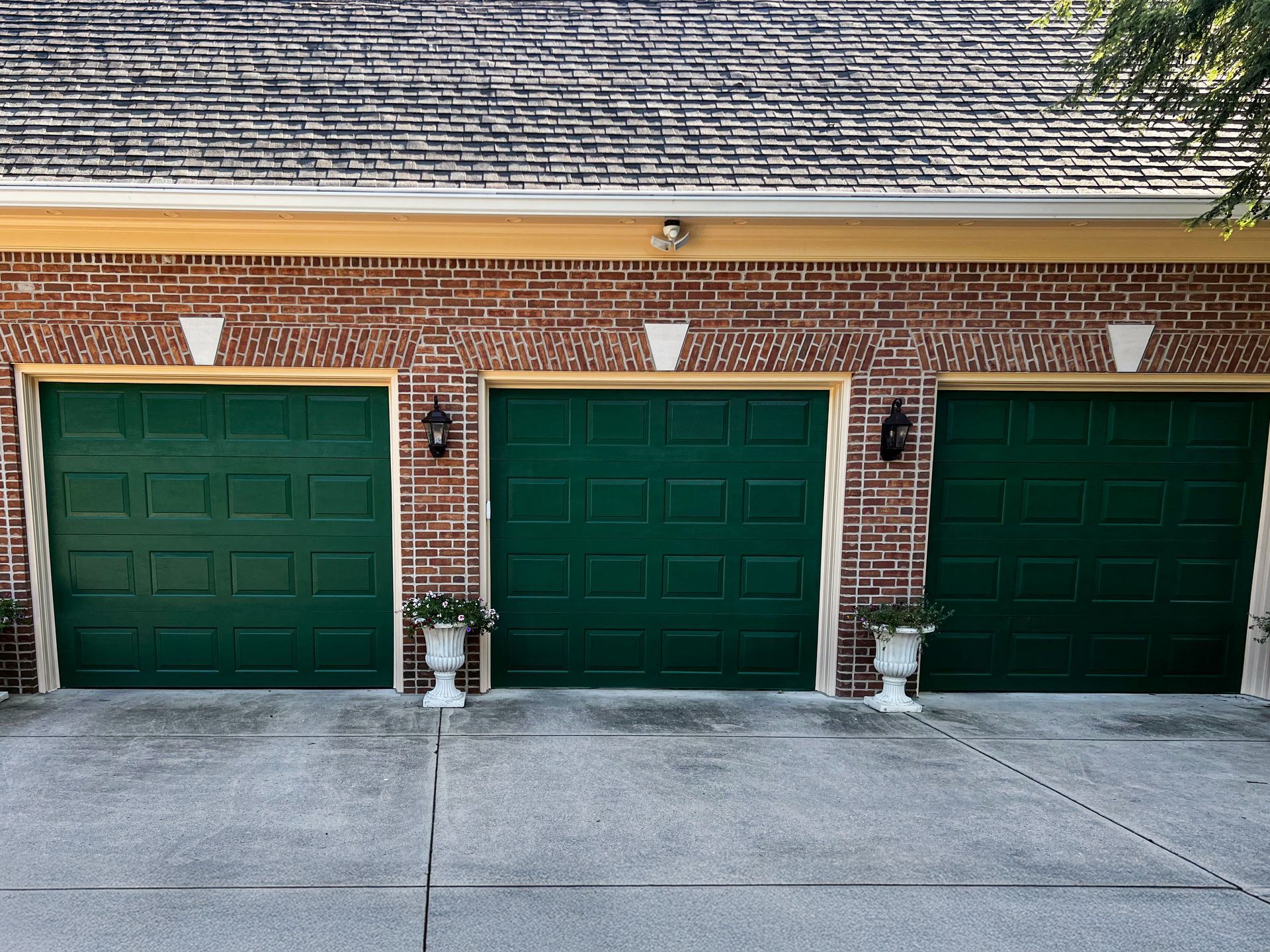 Three green garage doors on a brick house with white planters at the entrance of each bay.