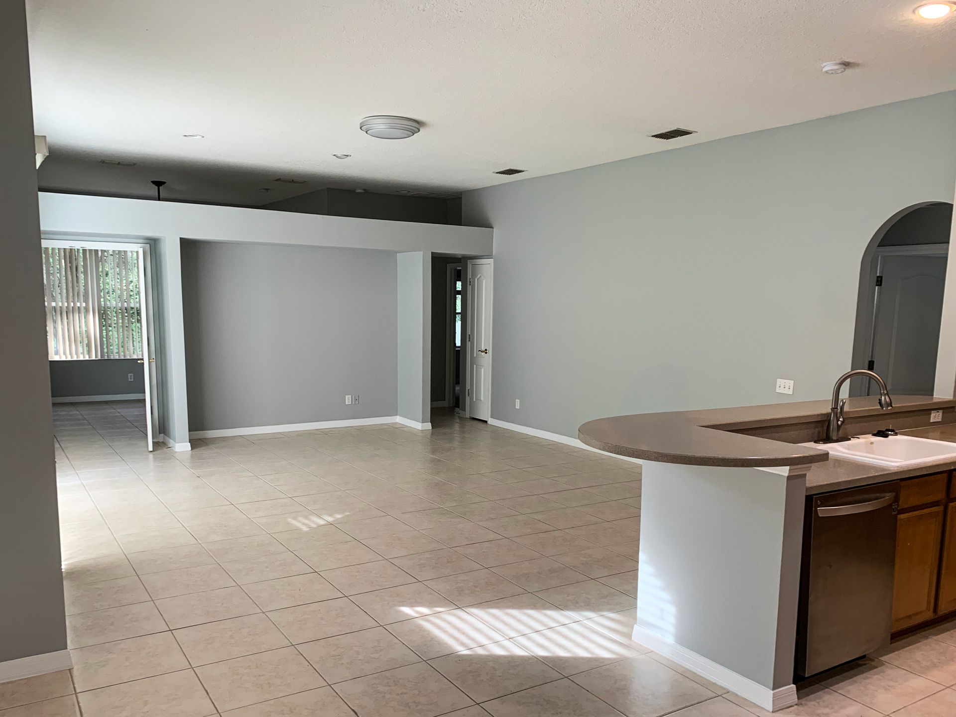 An open-concept living area with gray walls, light tiled floors, and a kitchen island with a stainless steel dishwasher.