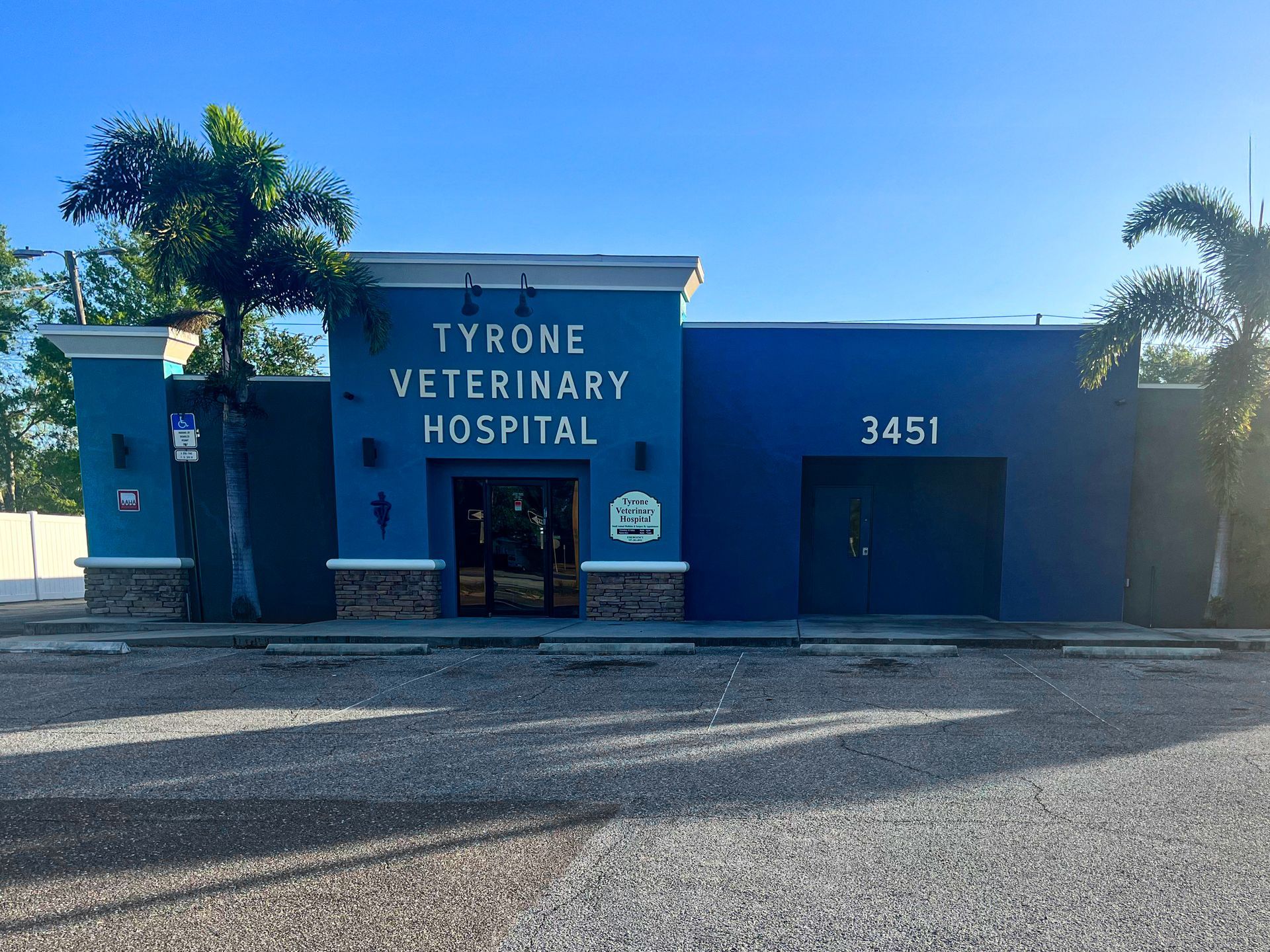 Blue, one-story Tyrone Veterinary Hospital building with address 3451, palm trees, and a gravel parking lot in front.