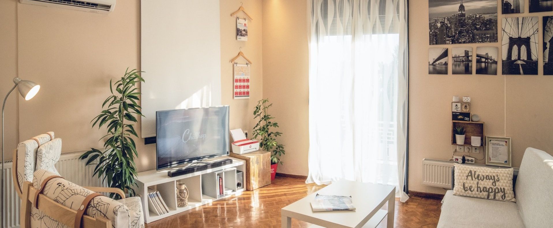 A cozy living room with a TV on a white stand, a coffee table, indoor plants, and a sofa with a decorative pillow.