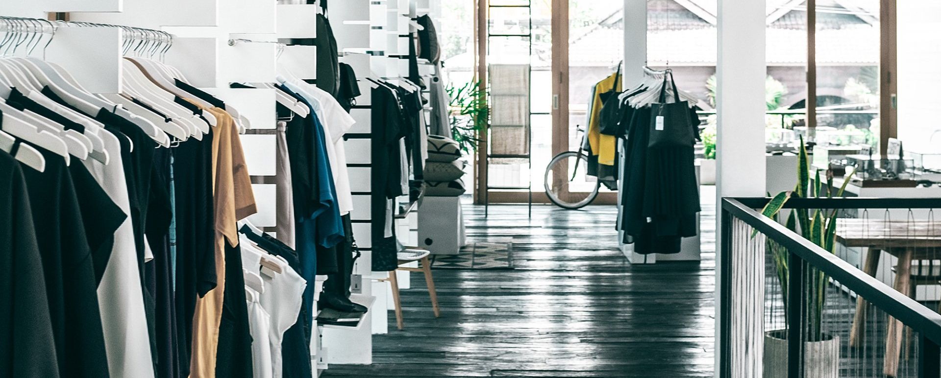 Racks of clothing in a minimalist, modern boutique with dark wooden floors and large windows.