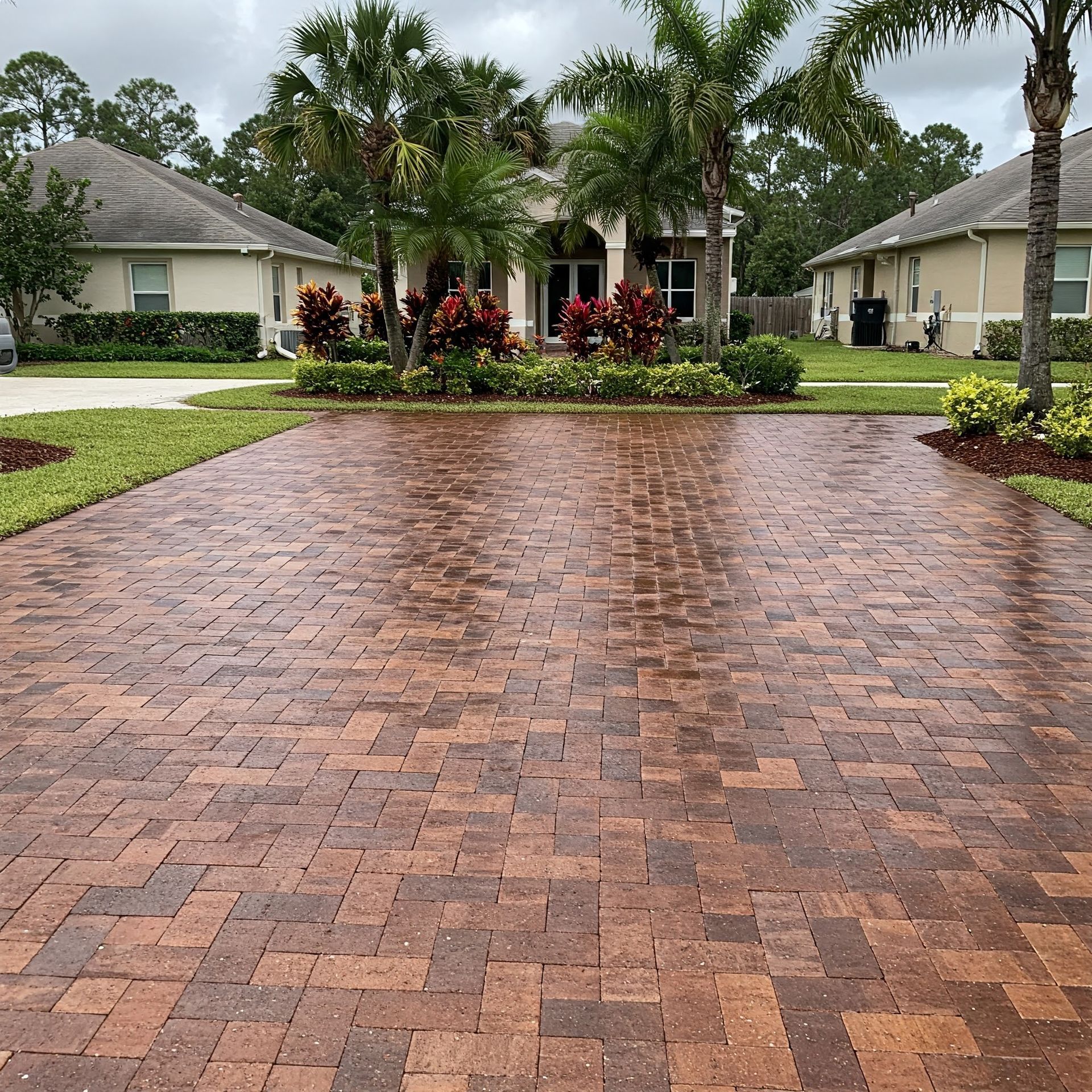 A brick driveway in front of a house with palm trees