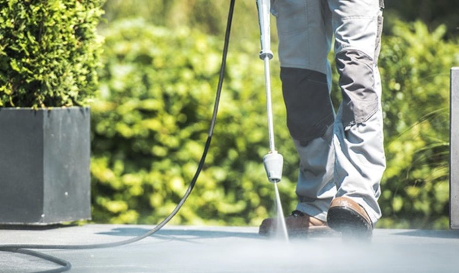 A person is using a high pressure washer to clean a patio.