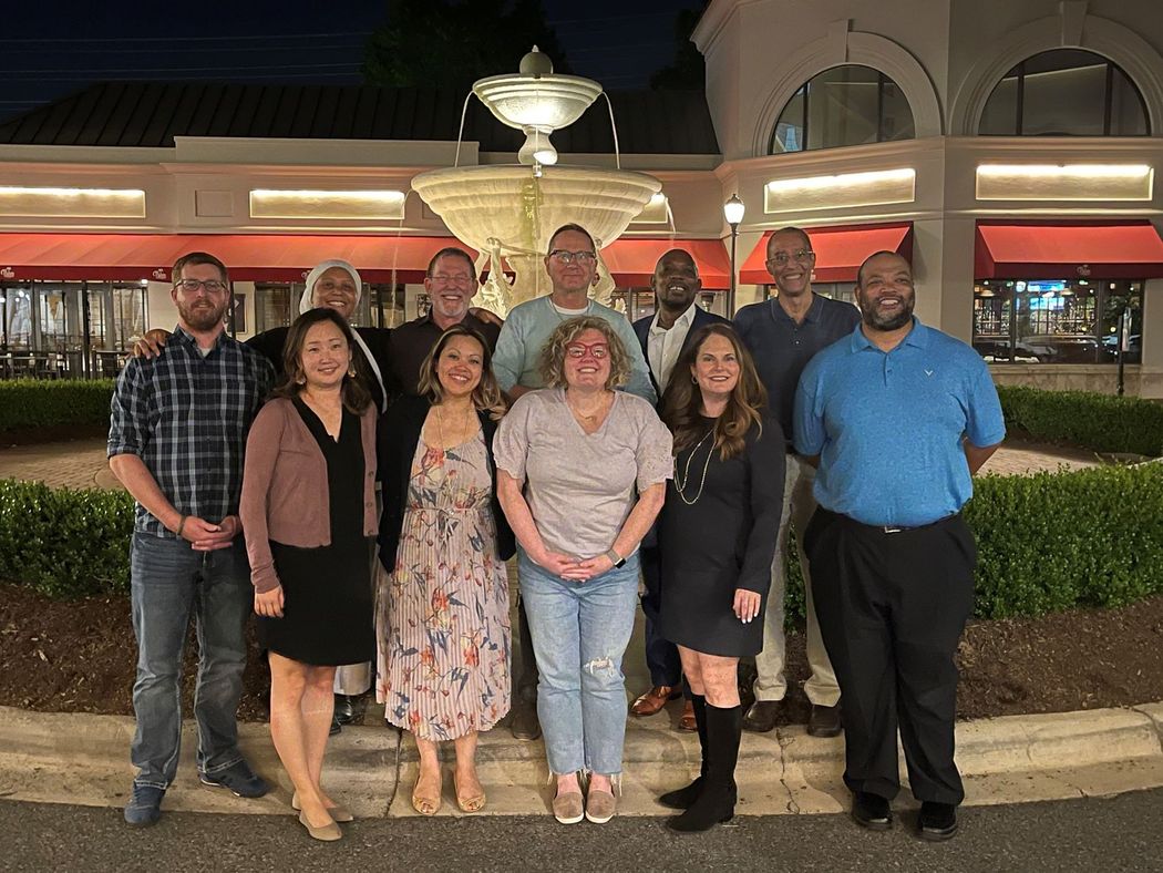 Group of people posing by a fountain at night, smiling. Building with red awnings in background.