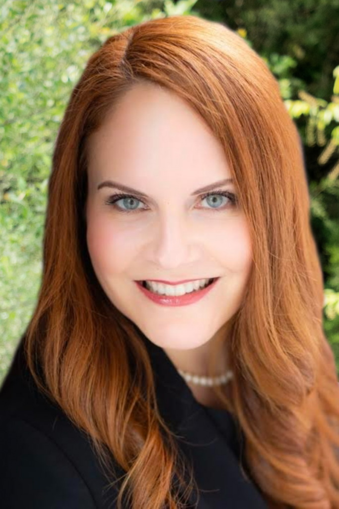 A woman with red hair and blue eyes is smiling for the camera.