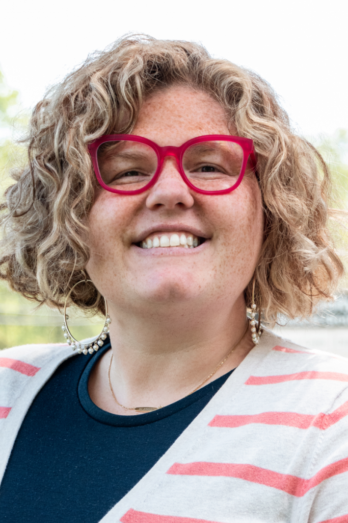 A woman wearing glasses and a striped sweater is smiling.