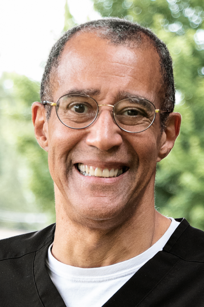 A man wearing glasses and a black shirt is smiling for the camera.