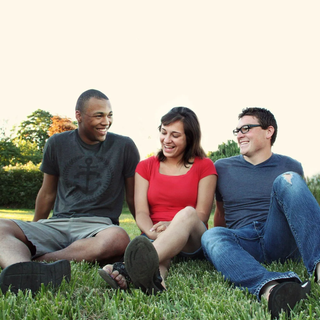 Two men and a woman are sitting in the grass and smiling