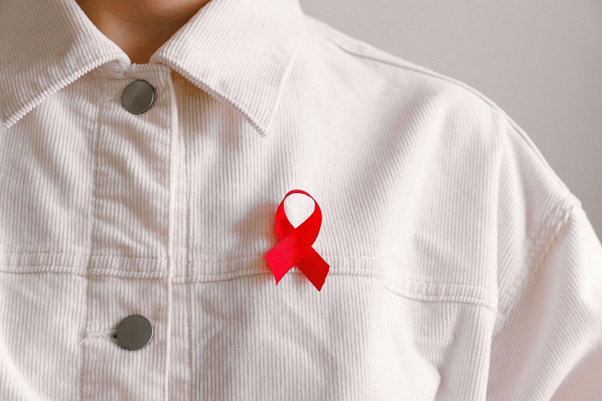 A woman wearing a white shirt with a red ribbon pinned to her chest.
