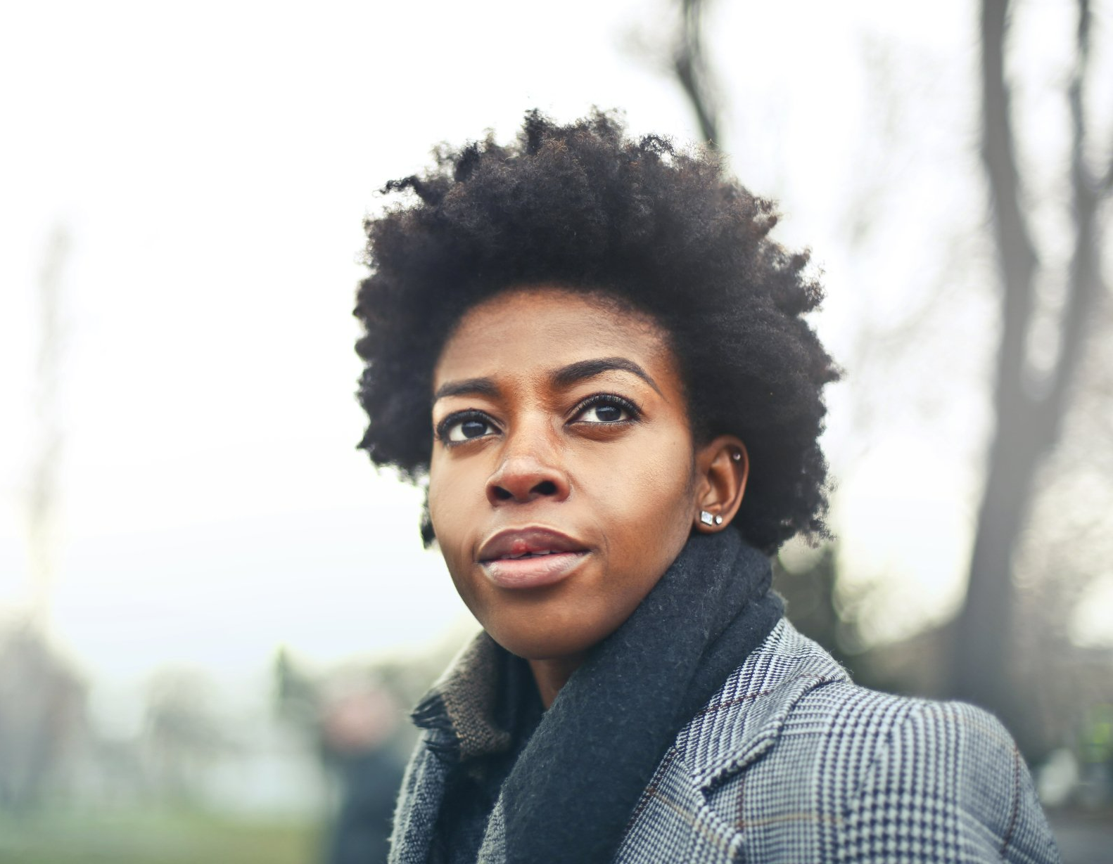 Una mujer con afro lleva un abrigo y una bufanda y mira a la cámara.
