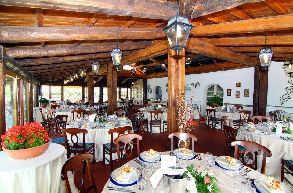 Interno di un ristorante con tavoli rotondi apparecchiati per cenare, travi in legno, lanterne.