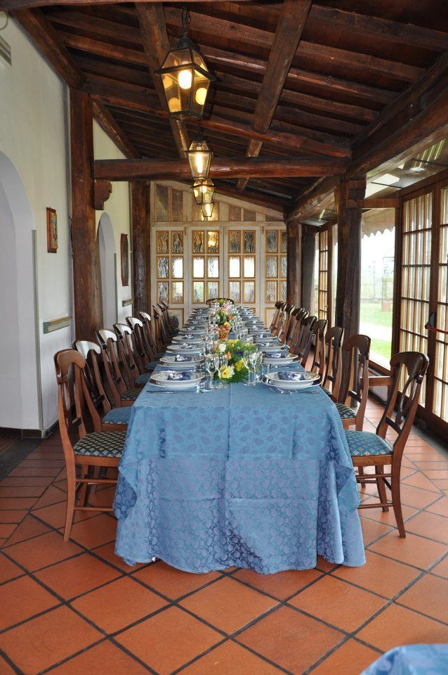 Lungo tavolo da pranzo apparecchiato per un pasto in una veranda con pavimento piastrellato e travi in legno.