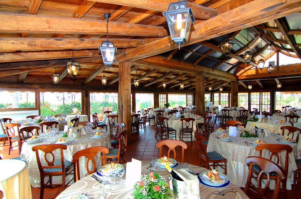 Interno del ristorante con tavoli rotondi apparecchiati per il pasto, travi in legno, finestre e lanterne appese.
