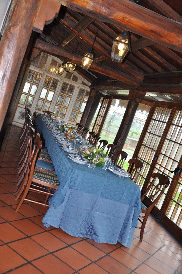 Lungo tavolo da pranzo apparecchiato per un pasto in una veranda con travi in legno e ampie finestre.