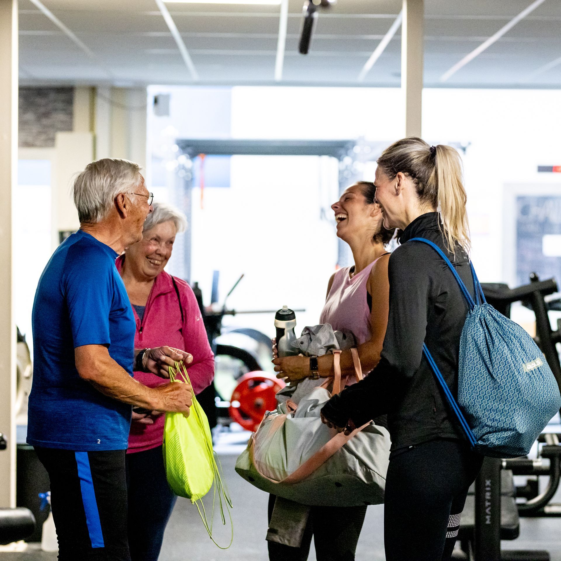 Vier mensen lachen samen in een sportschool. Twee oudere volwassenen, twee jongere vrouwen, lachend.