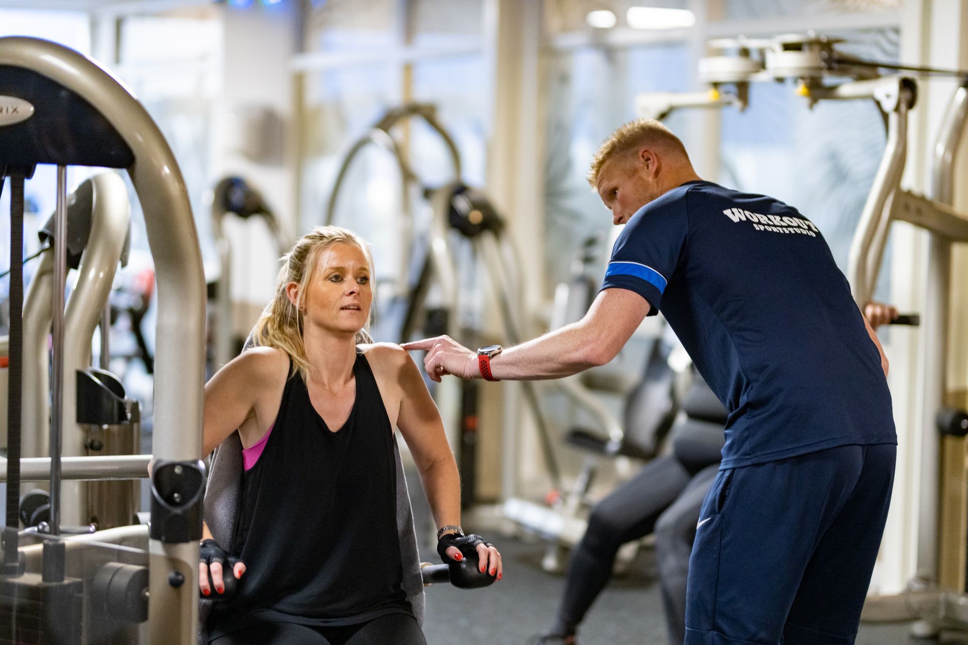 Een personal trainer helpt een vrouw op een borstdrukmachine in een sportschool.