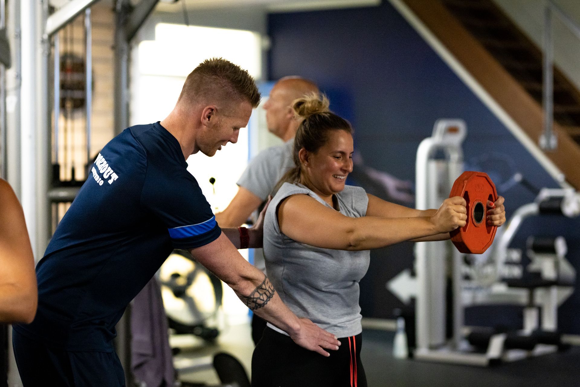 Een personal trainer helpt een vrouw bij het uitvoeren van een oefening met gewichten in de sportschool.