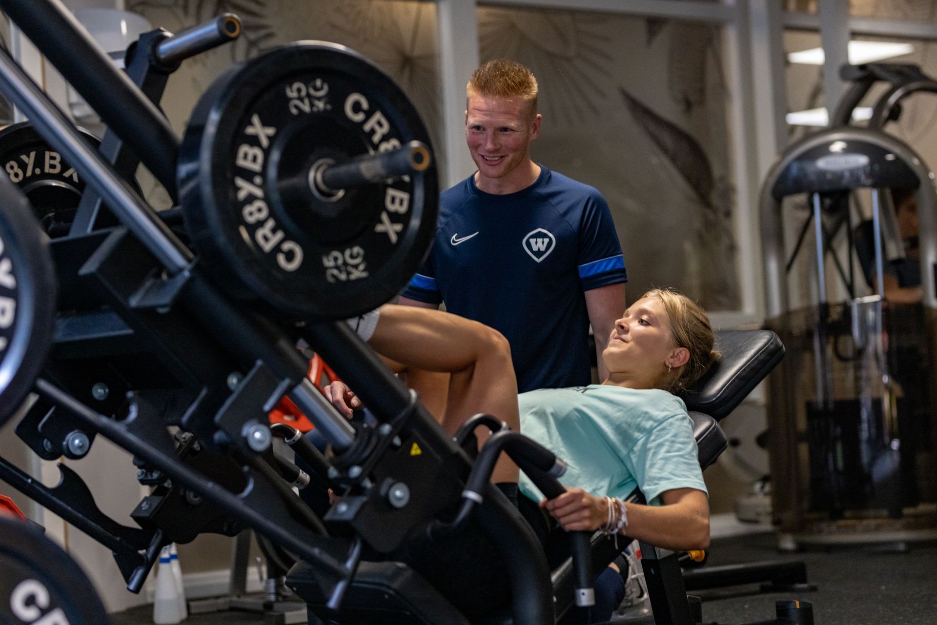 Een vrouw doet leg presses met een trainer. Ze zijn in de sportschool.