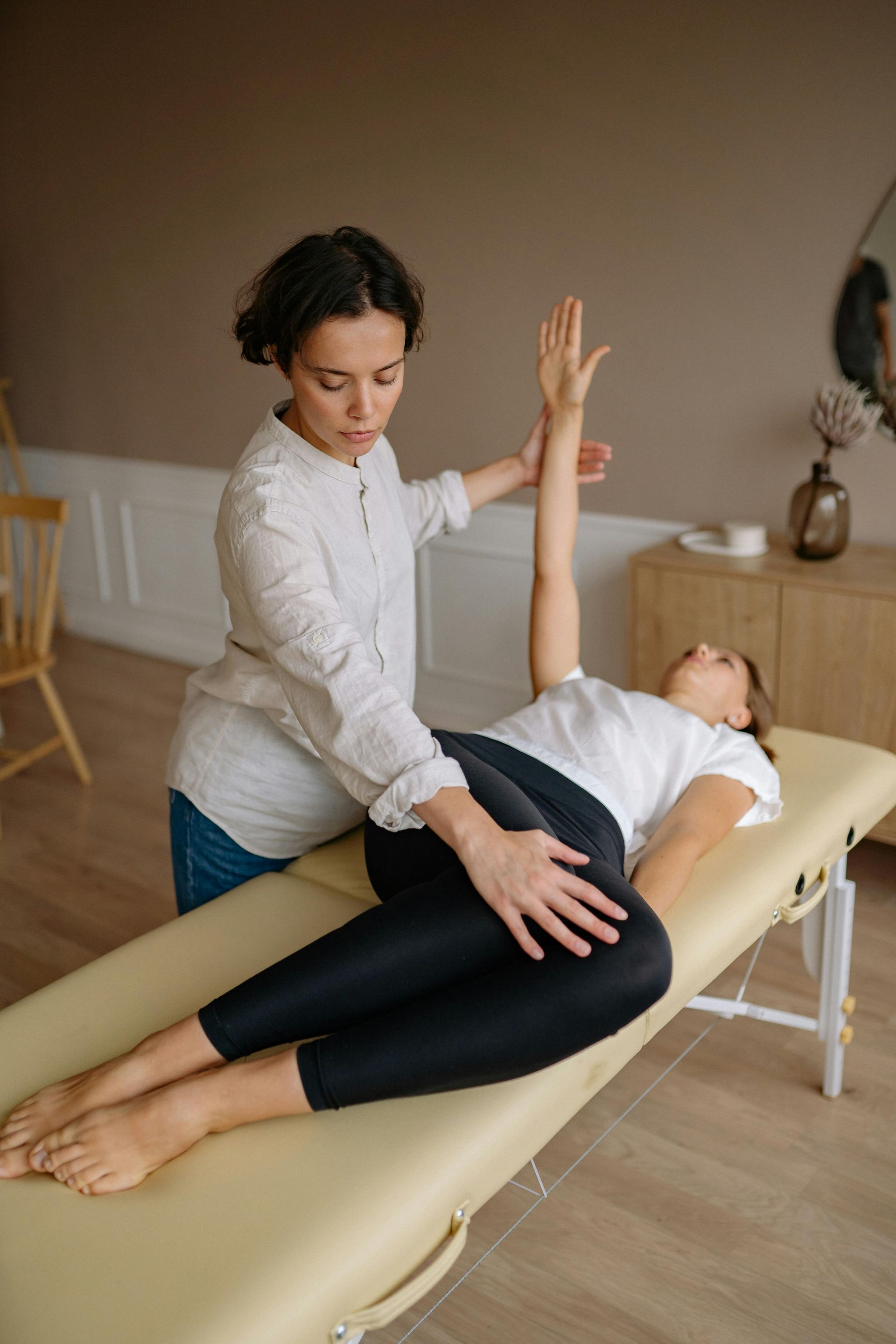Vrouw krijgt fysiotherapie op een massagetafel. De therapeut heft haar arm op en oefent druk uit op haar heup.