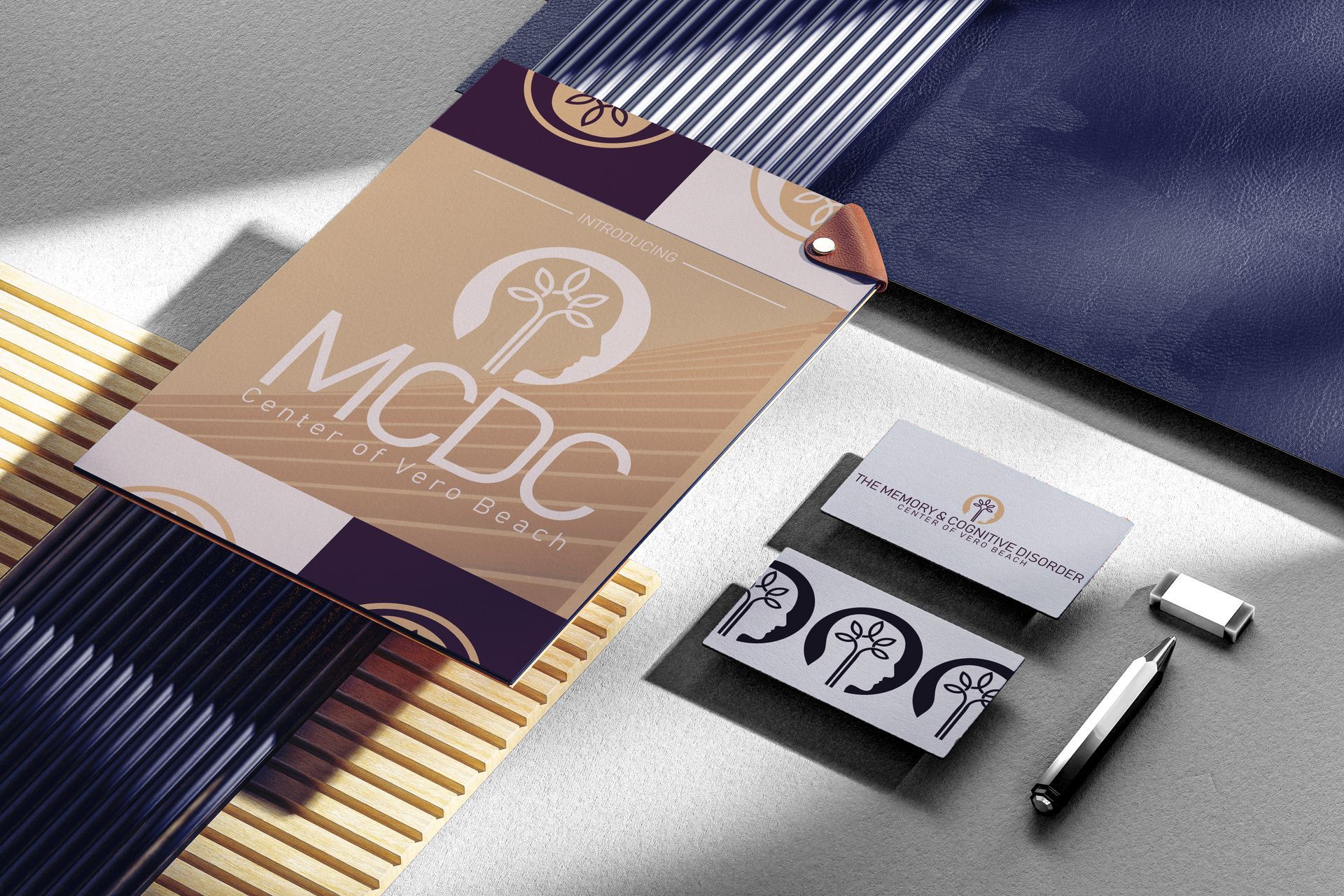Business card set with stationery by PGM. The MCDC logo is on a folder, business cards, and pen on a patterned surface.