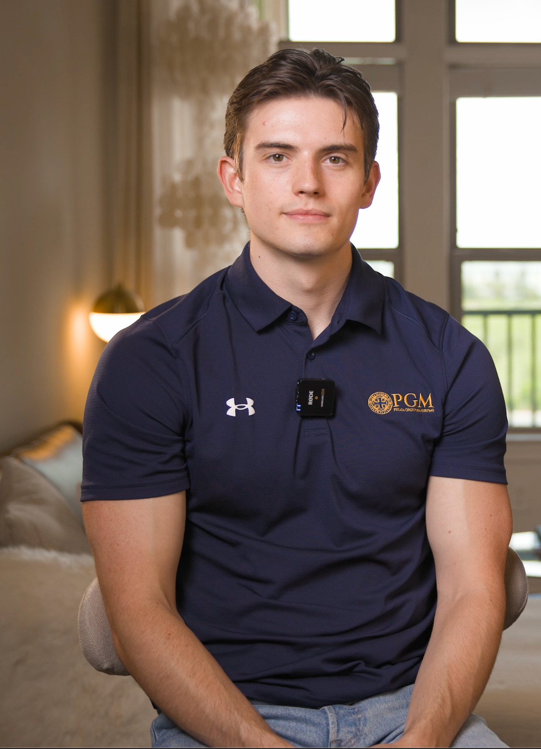 Man in navy polo shirt seated indoors, facing the camera with a neutral expression.