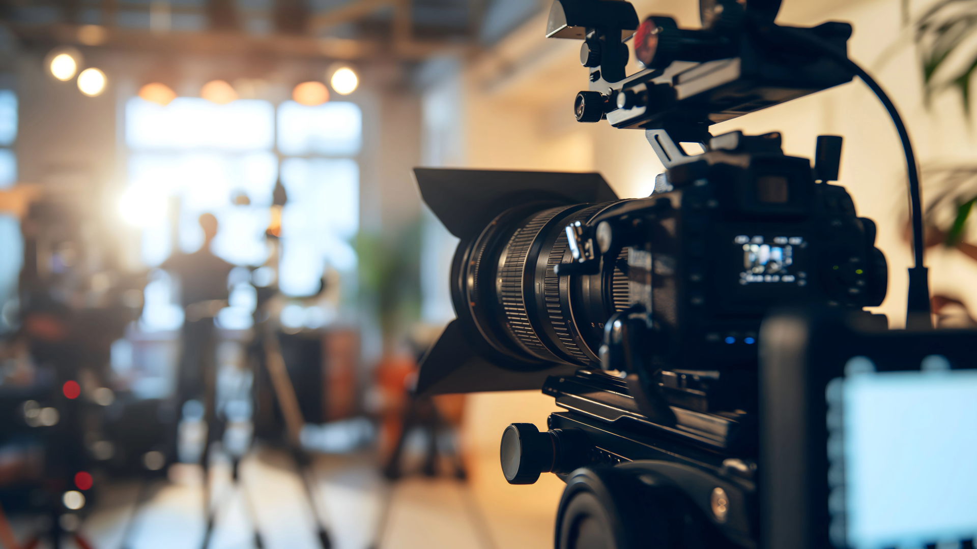Professional cinema camera on a tripod, focused on a blurred, sunlit studio production set.