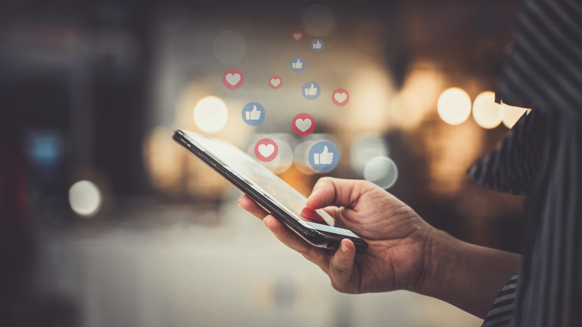 Close-up of a person holding a smartphone with social media like and heart icons floating above the screen.