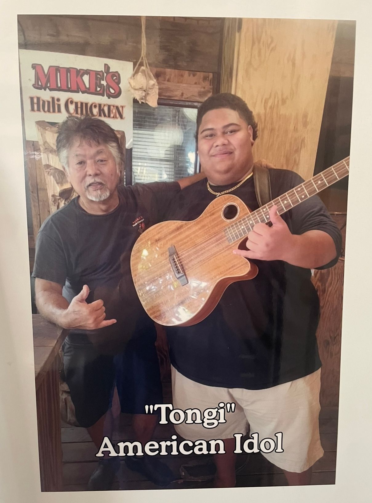Two men posing at Mike's Huli Chicken restaurant. One, holding a ukulele, is identified as 