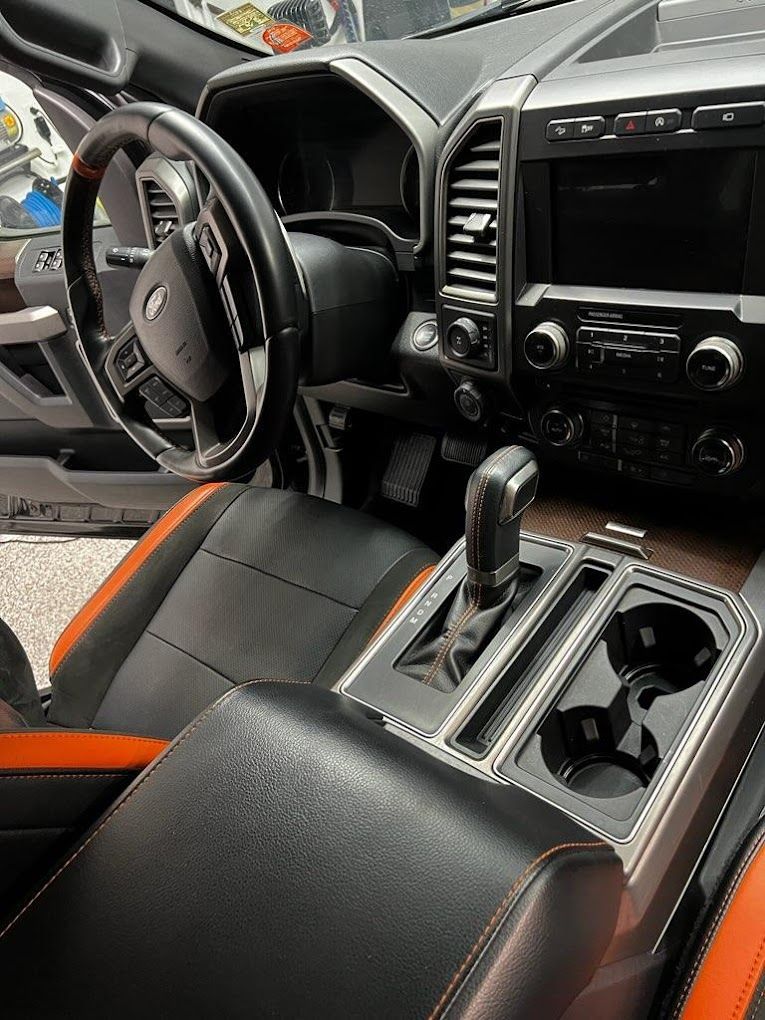The interior of a ford f150 raptor with black and orange seats and a steering wheel.