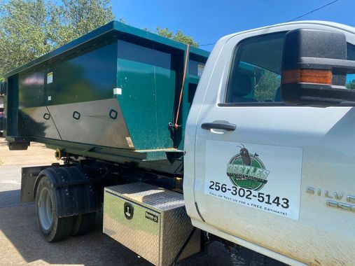 White utility truck towing a green dump trailer, parked outdoors on a sunny day.