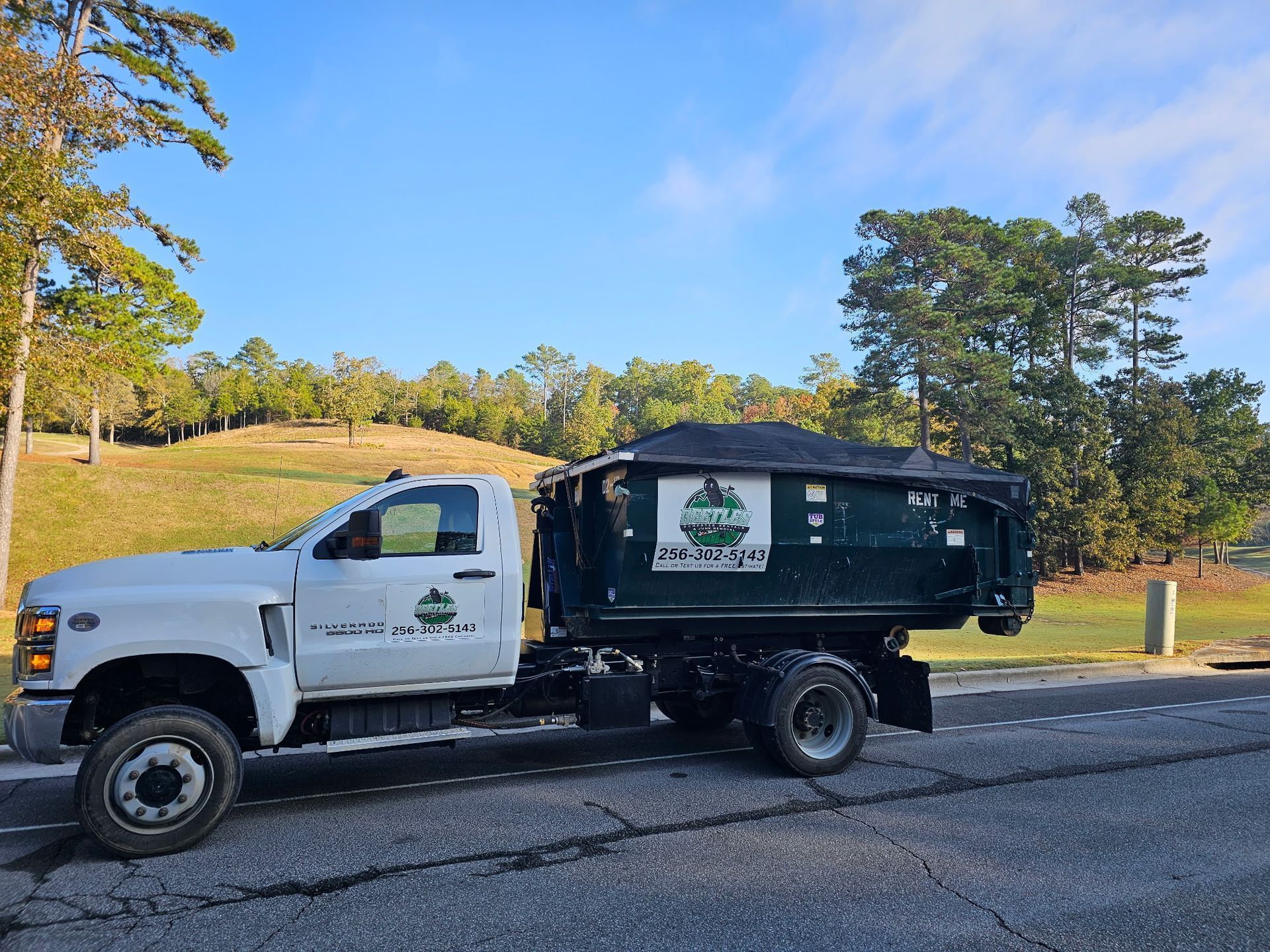 White work truck with black dump bed parked on a road beside a grassy field and trees