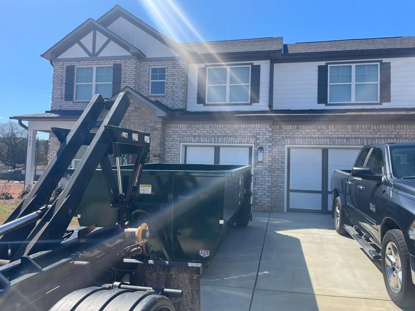 Two-story house with a truck and black trailer parked in the driveway on a sunny day