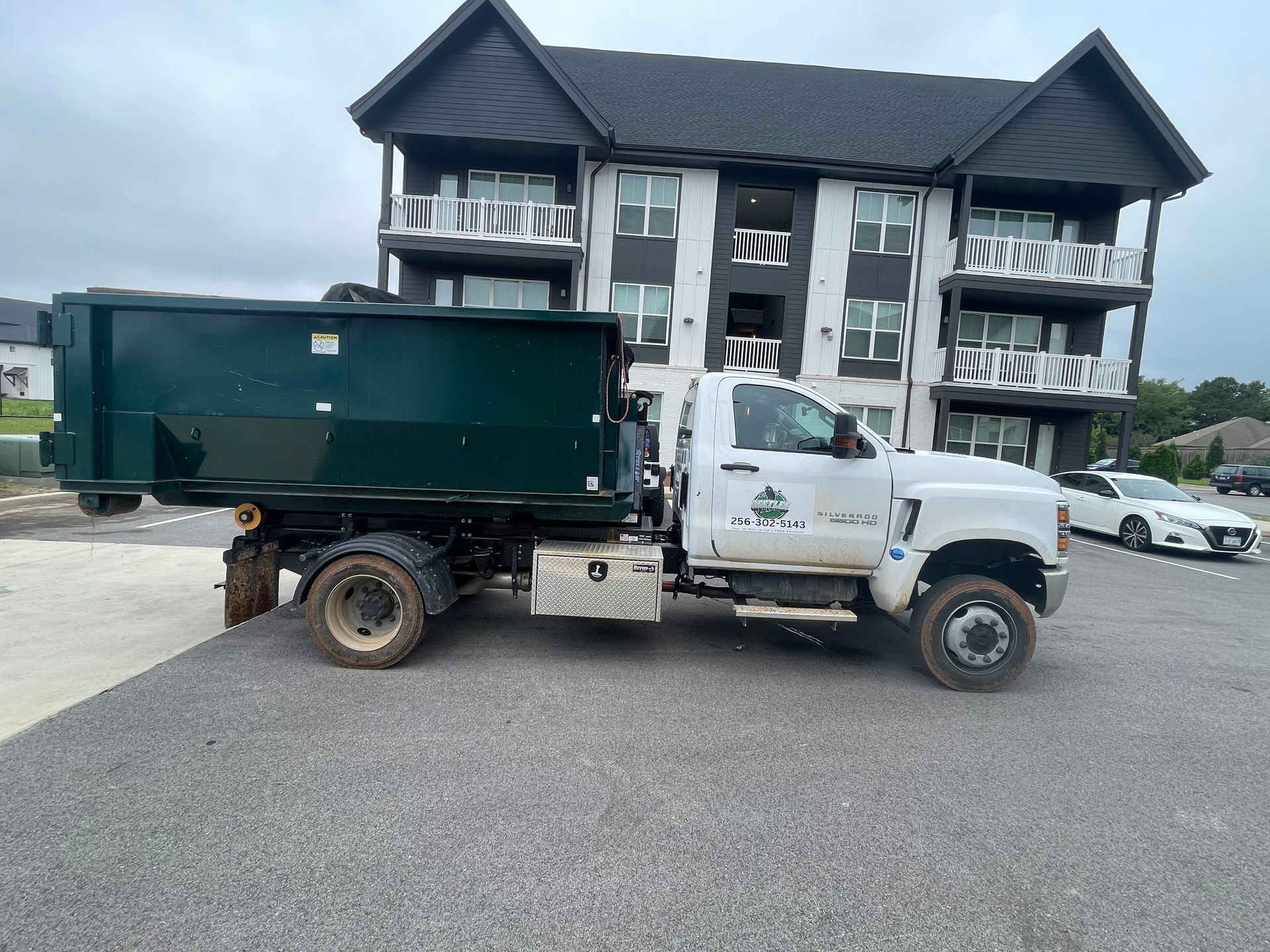 White dump truck with green cargo bed parked in front of a dark apartment building.
