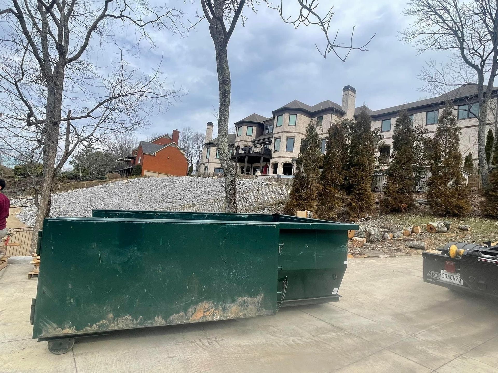 Green dumpster in a courtyard with apartment buildings and bare trees in the background