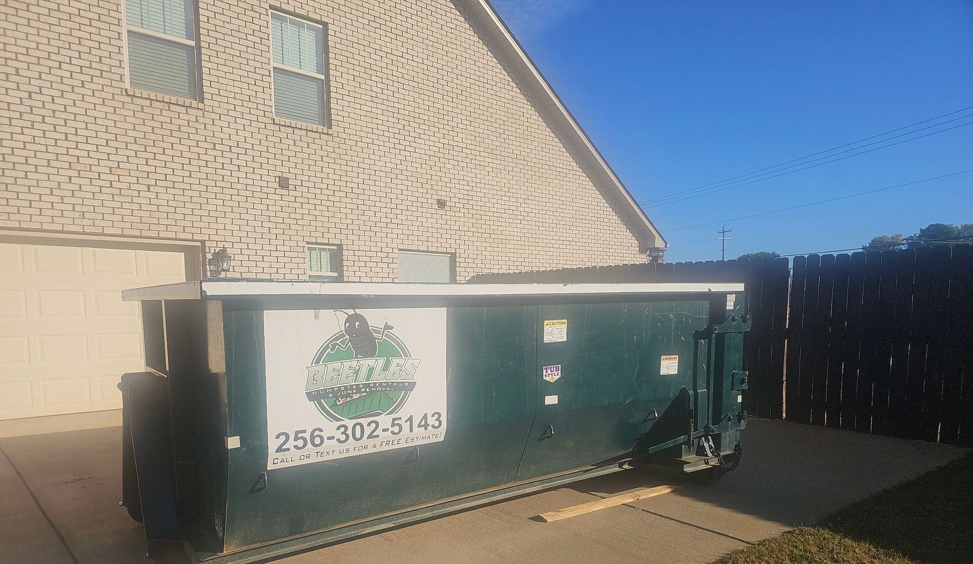 Green dumpster beside a house with a white sign on the side under a blue sky