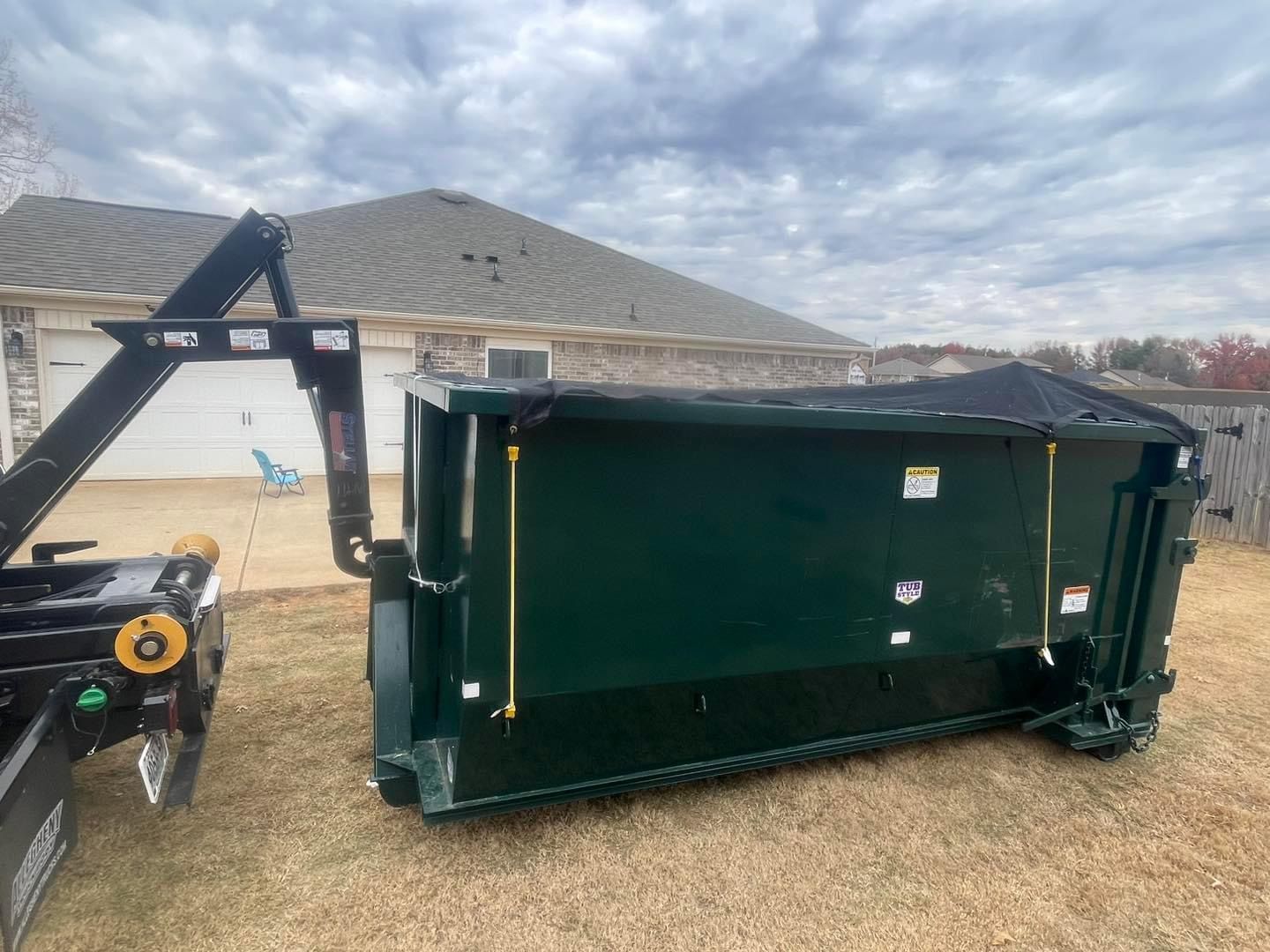 Large green dumpster being lifted by a front loader in a residential yard