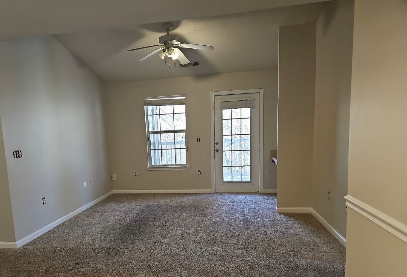 Empty carpeted living room with ceiling fan, window, and glass door leading outside