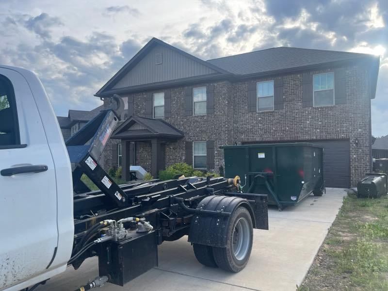 White utility truck with raised chassis parked in a driveway beside a brick two-story house.