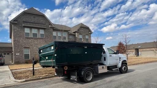 White dump truck parked on a residential street in front of a brick house under a cloudy sky