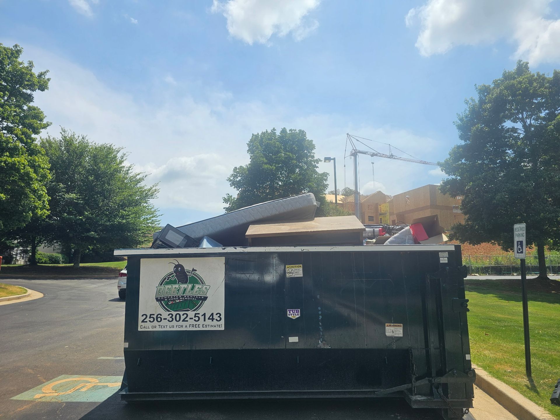Black dumpster filled with debris in a parking lot on a sunny day