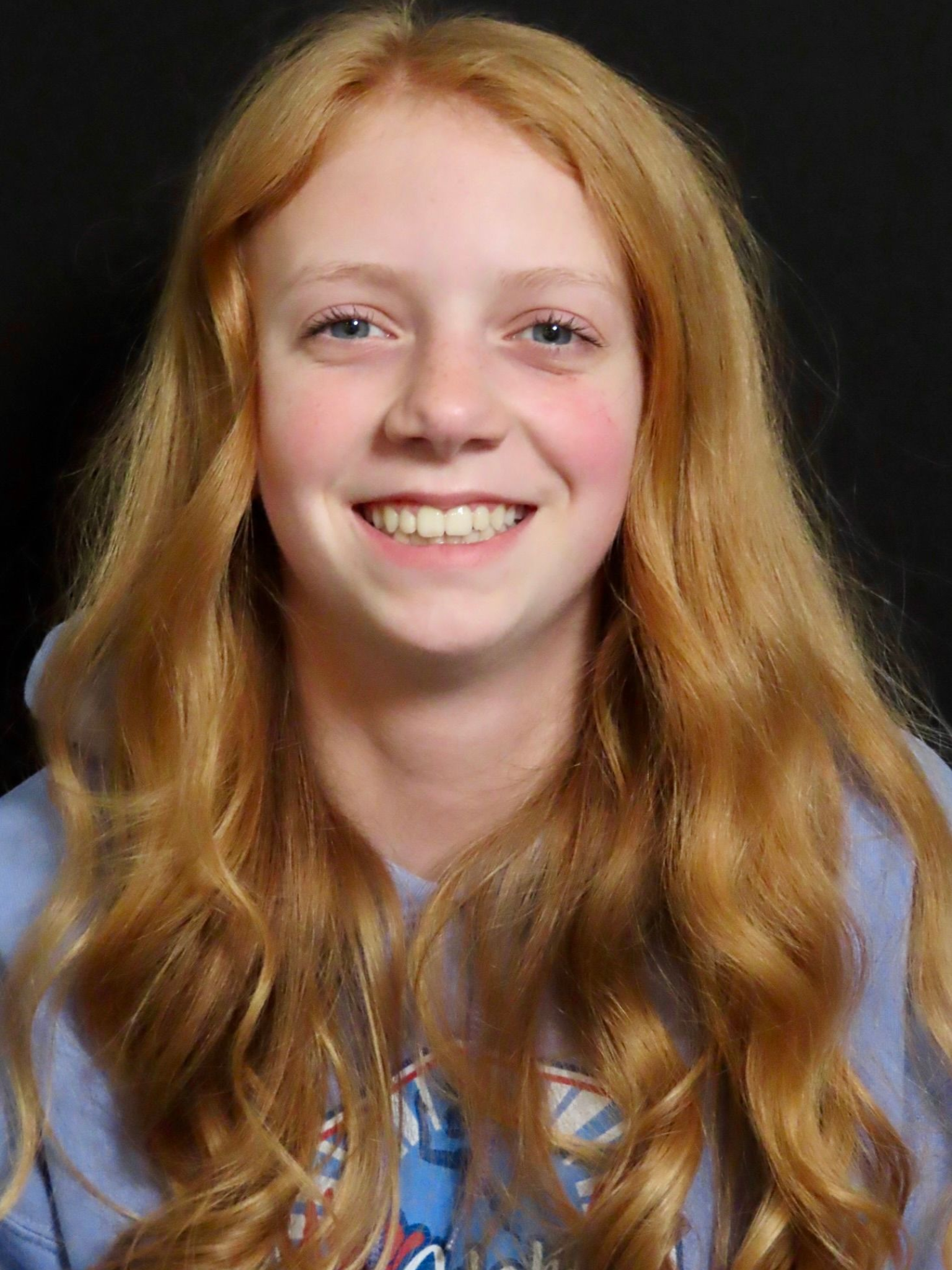 Smiling person with long red hair against a black background, wearing a blue shirt