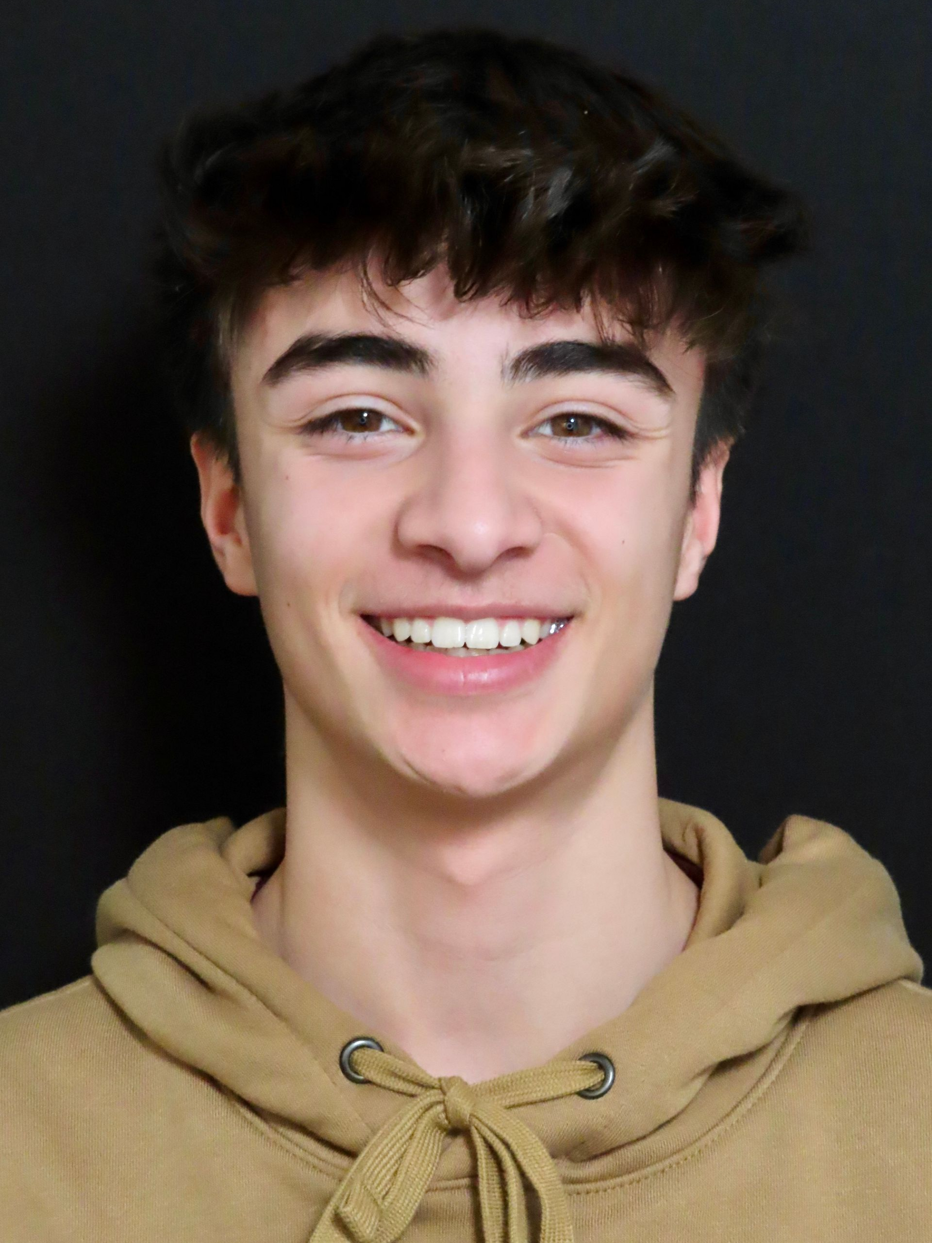 Smiling young person in a tan hoodie against a dark background