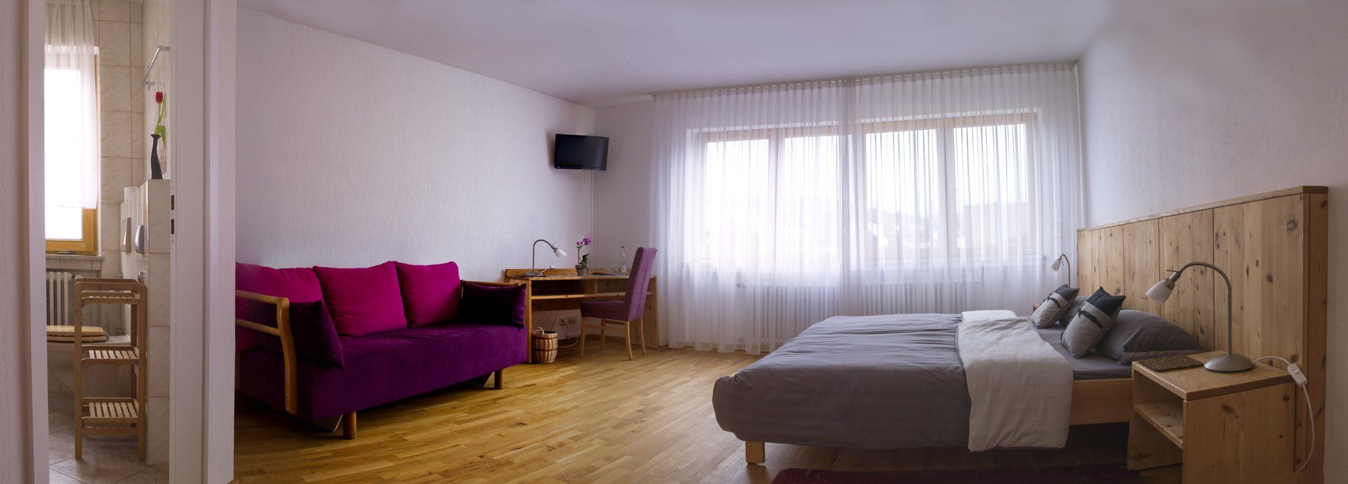 zimmer im haus am weingarten mit bordeauxroten sofa doppelbett, schreibtisch und viel natürlichem licht